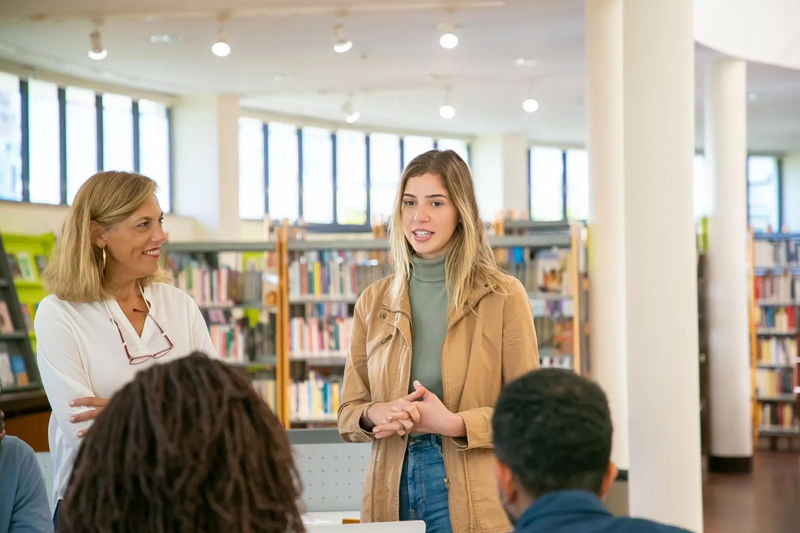 Una joven presenta de pie ante otras personas en una biblioteca