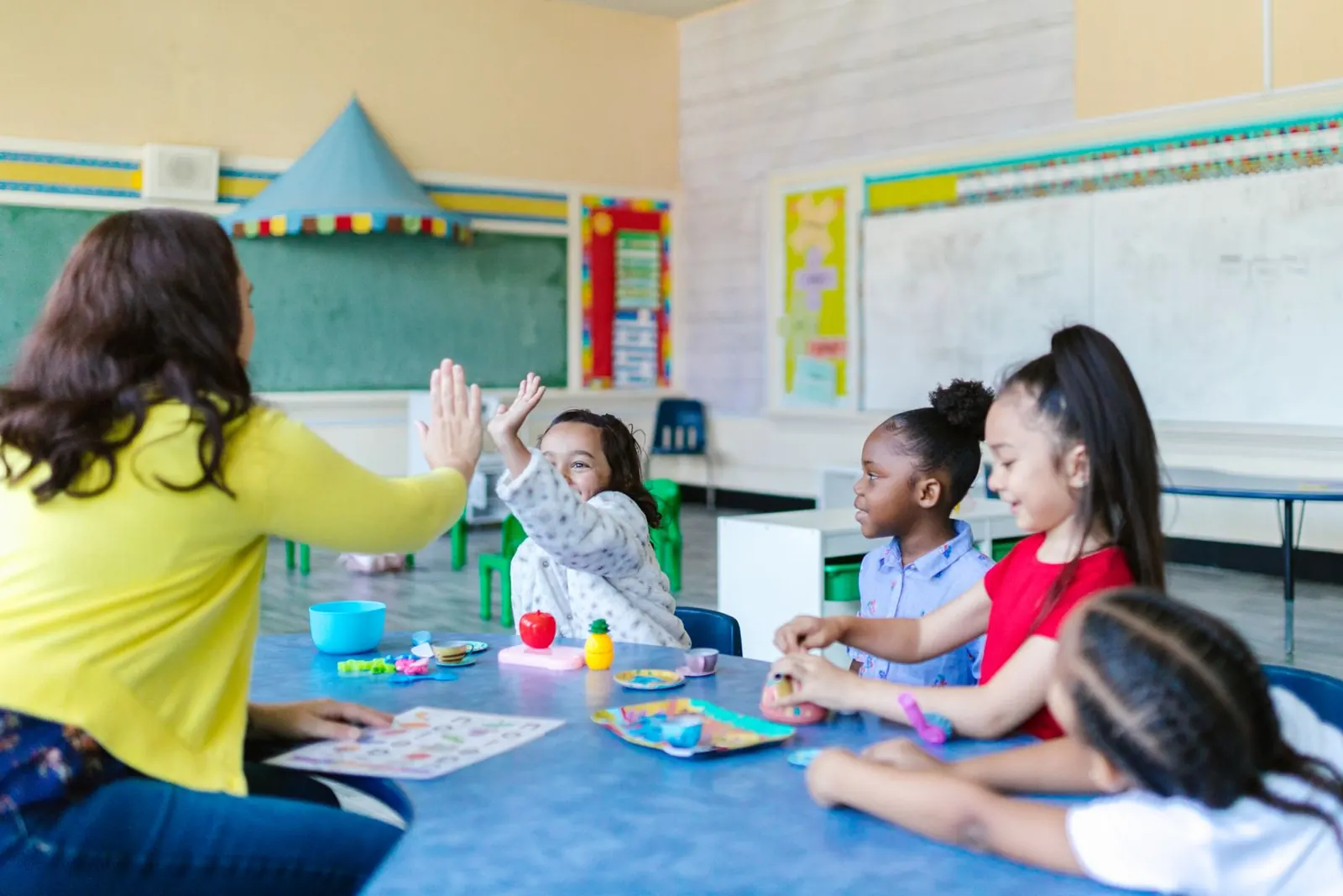 Una docente choca la mano con una alumna en un aula de infantil